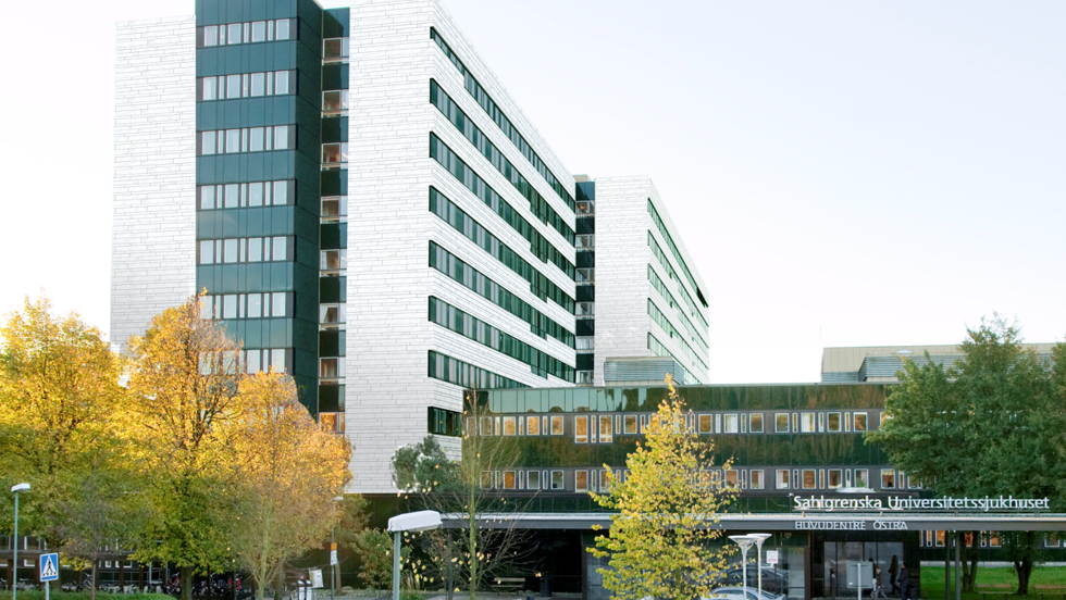 gestaltningsbild av vitt och grönt sjukhus med höstgula träd i förgrunden.