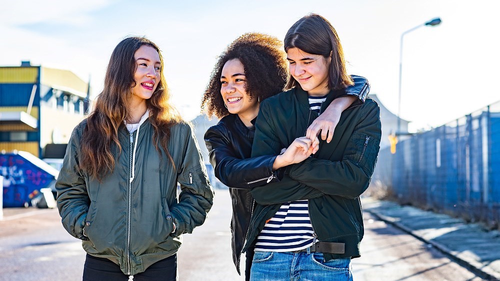 Tre ungdomar håller om varandra och ler.